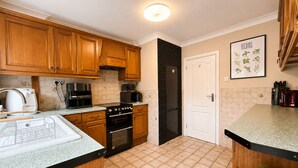 A modern kitchen with wooden cabinets, a black refrigerator, a coffee machine, and a tiled floor. - Spacious 4BDR Home in Rayleigh Essex (Essex)