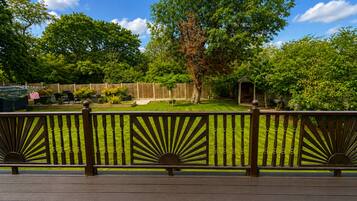 Une terrasse en bois avec une balustrade ornée d’un motif en forme de soleil, donnant sur une cour arrière bien entretenue, avec une pelouse, des arbres et une clôture en bois.