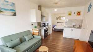 A compact living space with a sofa, a small wooden table, a kitchenette, and a bed. - The Ocean House - Sea Shell (Hunstanton)
