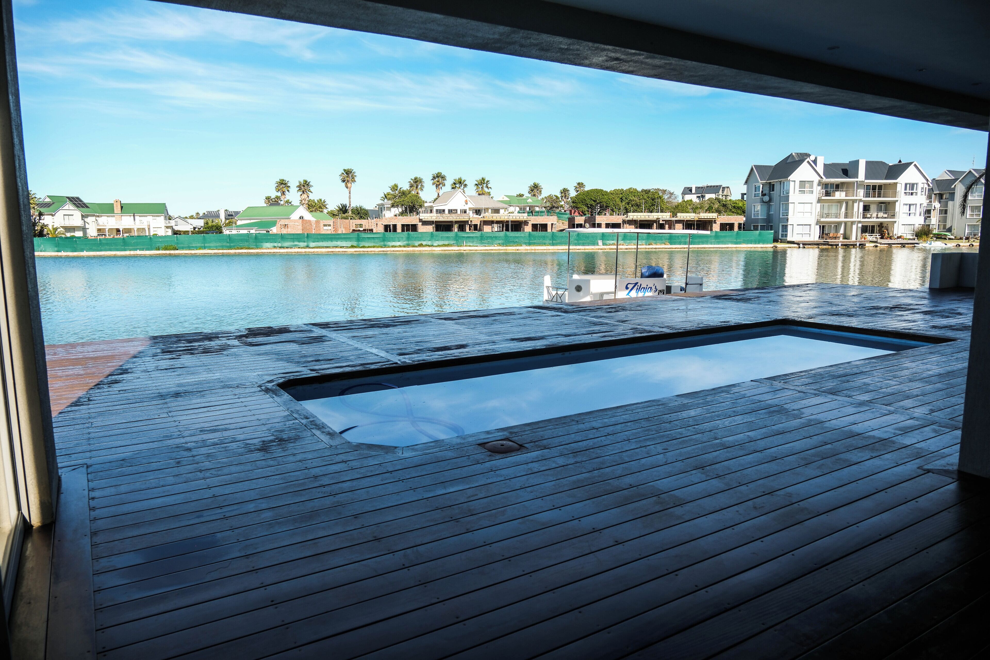 A wooden deck with a hot tub, a view of a calm body of water, and buildings in the background.