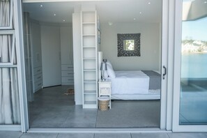Ein Schlafzimmer mit Bett, Nachttisch, Lampe, kleiner Korbtasche, Fenster mit Blick und Kleiderschrank.