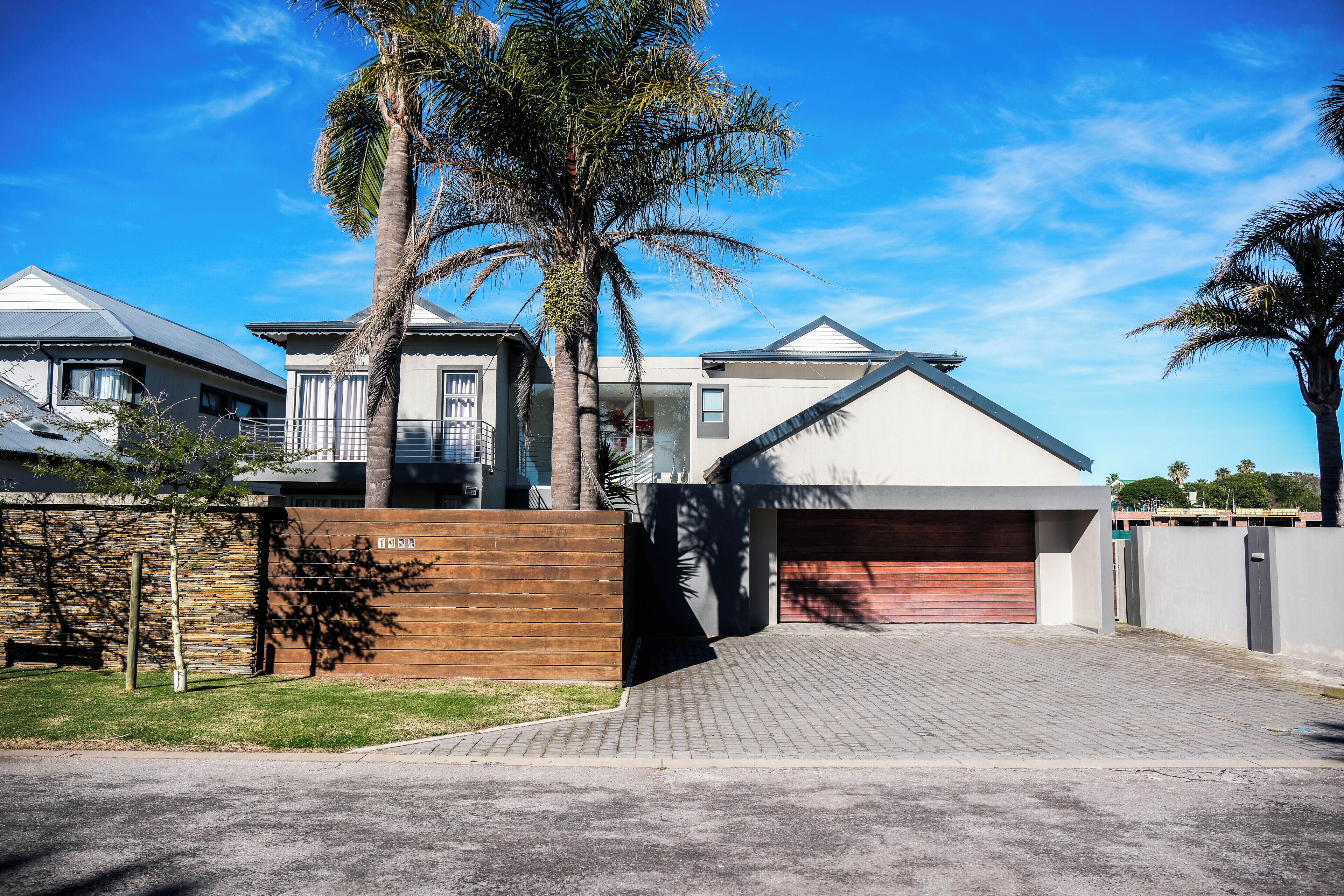 A modern two-story house with a garage, a wooden fence, and a palm tree.