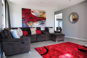 A modern living room with a sectional sofa, a red rug, and a large abstract painting. - 
Your perfect Beach Escape in Zifaja Living Marina, Relax and Make Memories (Jeffreys Bay)