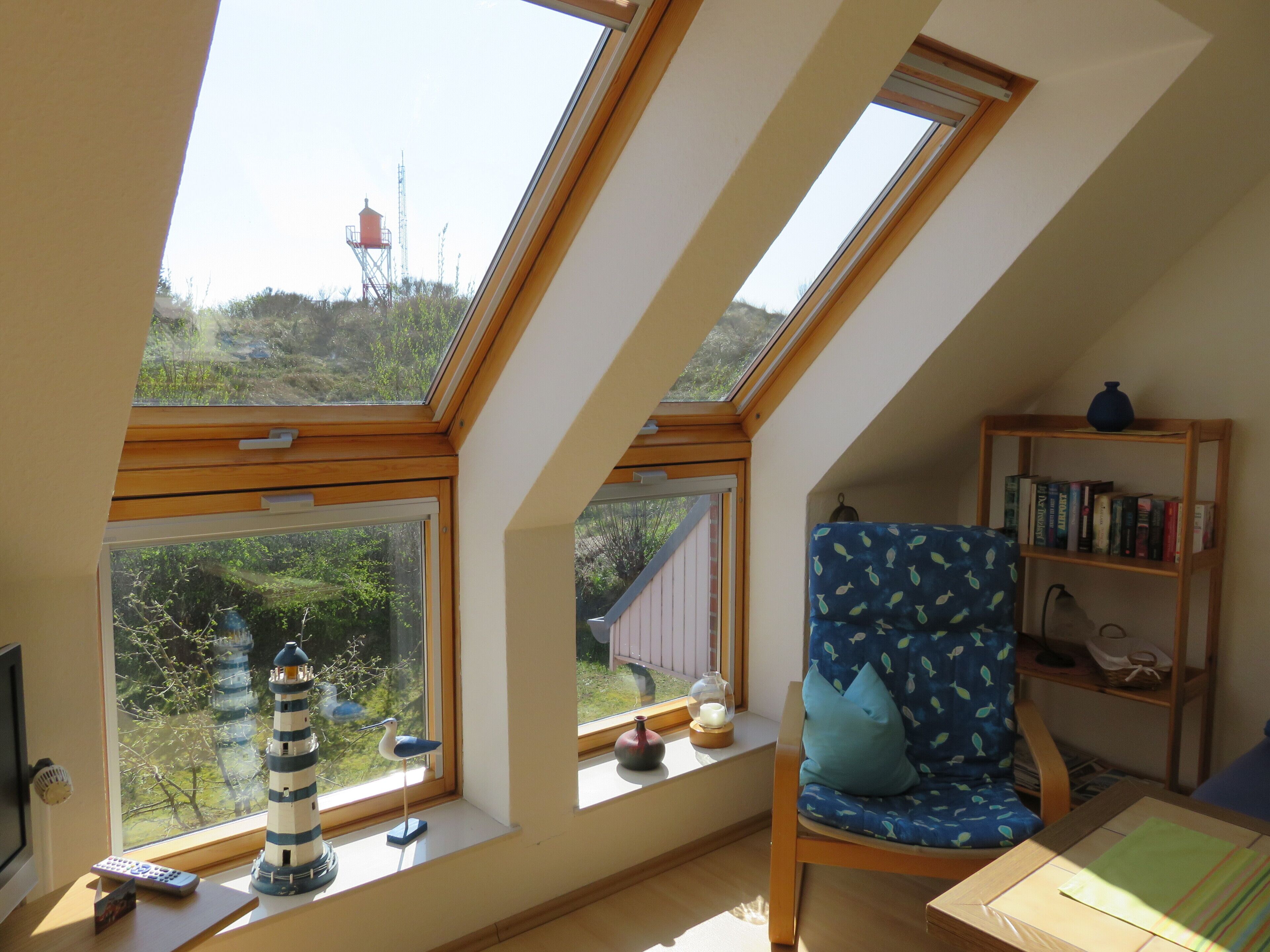 Une pièce dotée de fenêtres de toit, d’une chaise, d’une bibliothèque et d’une petite table.