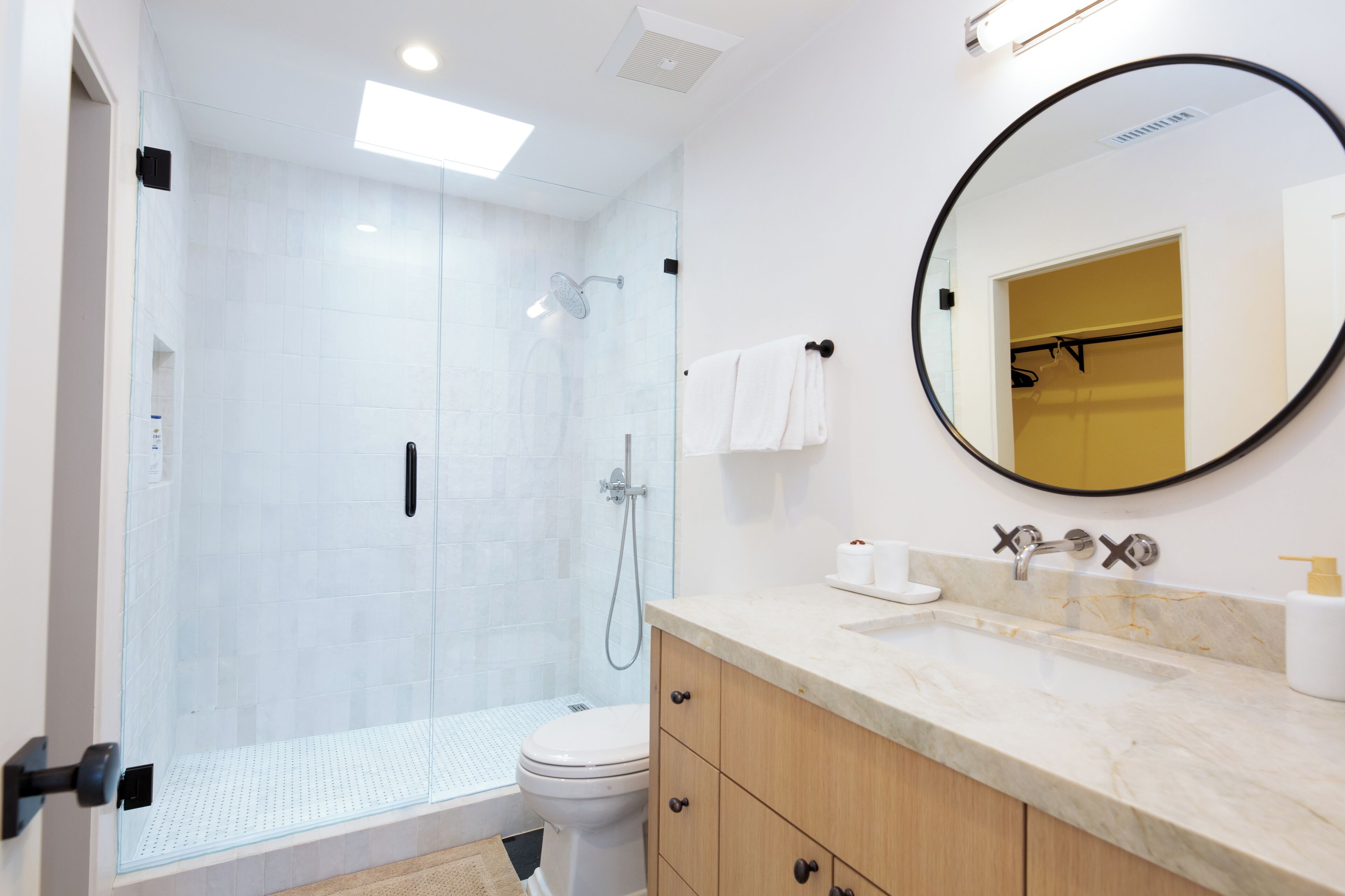 A modern bathroom with a glass-enclosed shower, a toilet, and a vanity with a mirror.