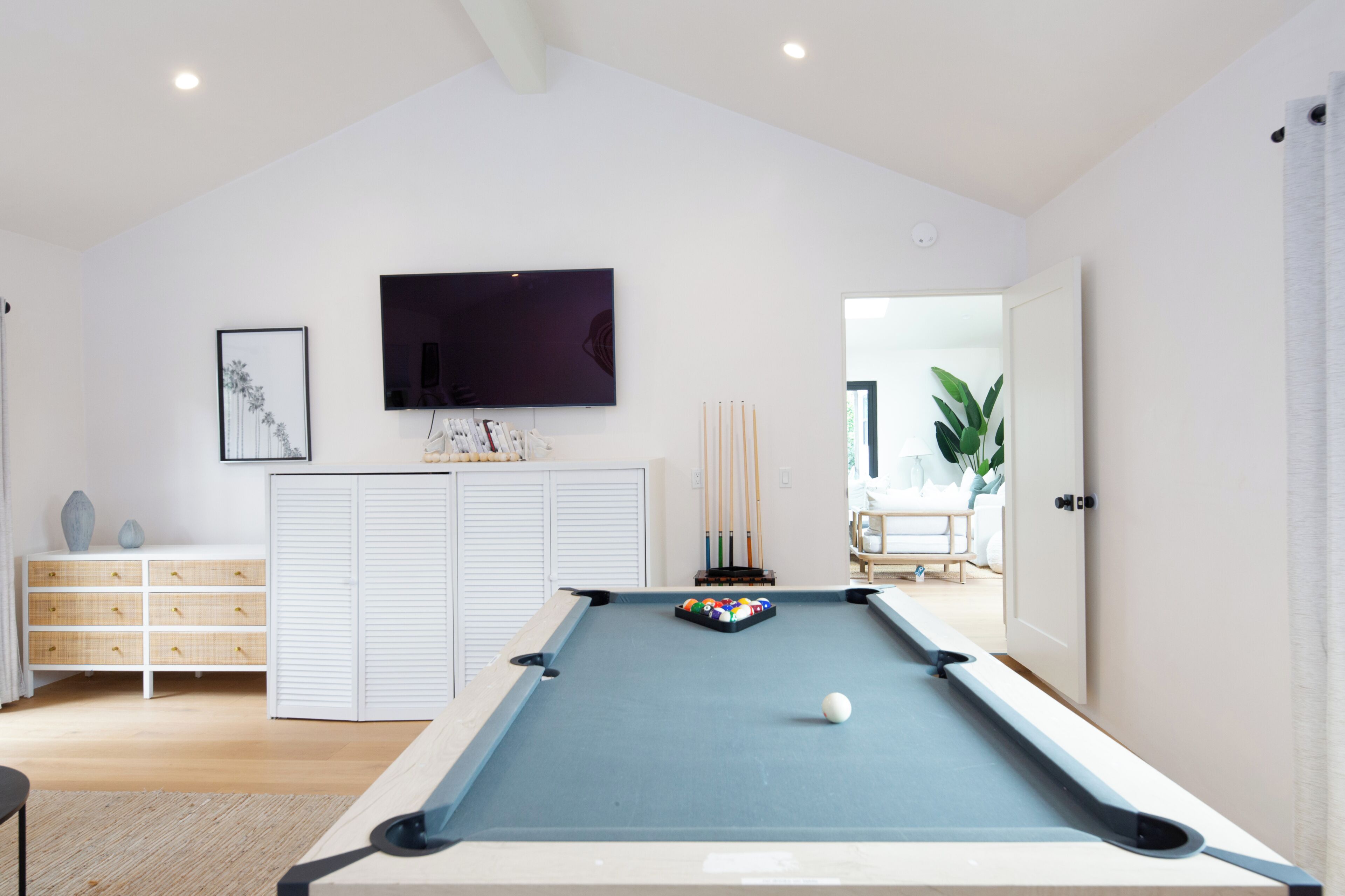 Une table de billard dans une pièce où l’on trouve un téléviseur fixé au mur, une commode et un tableau encadré.