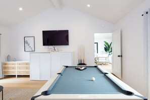 A pool table in a room with a television mounted on the wall, a set of drawers, and a framed picture.