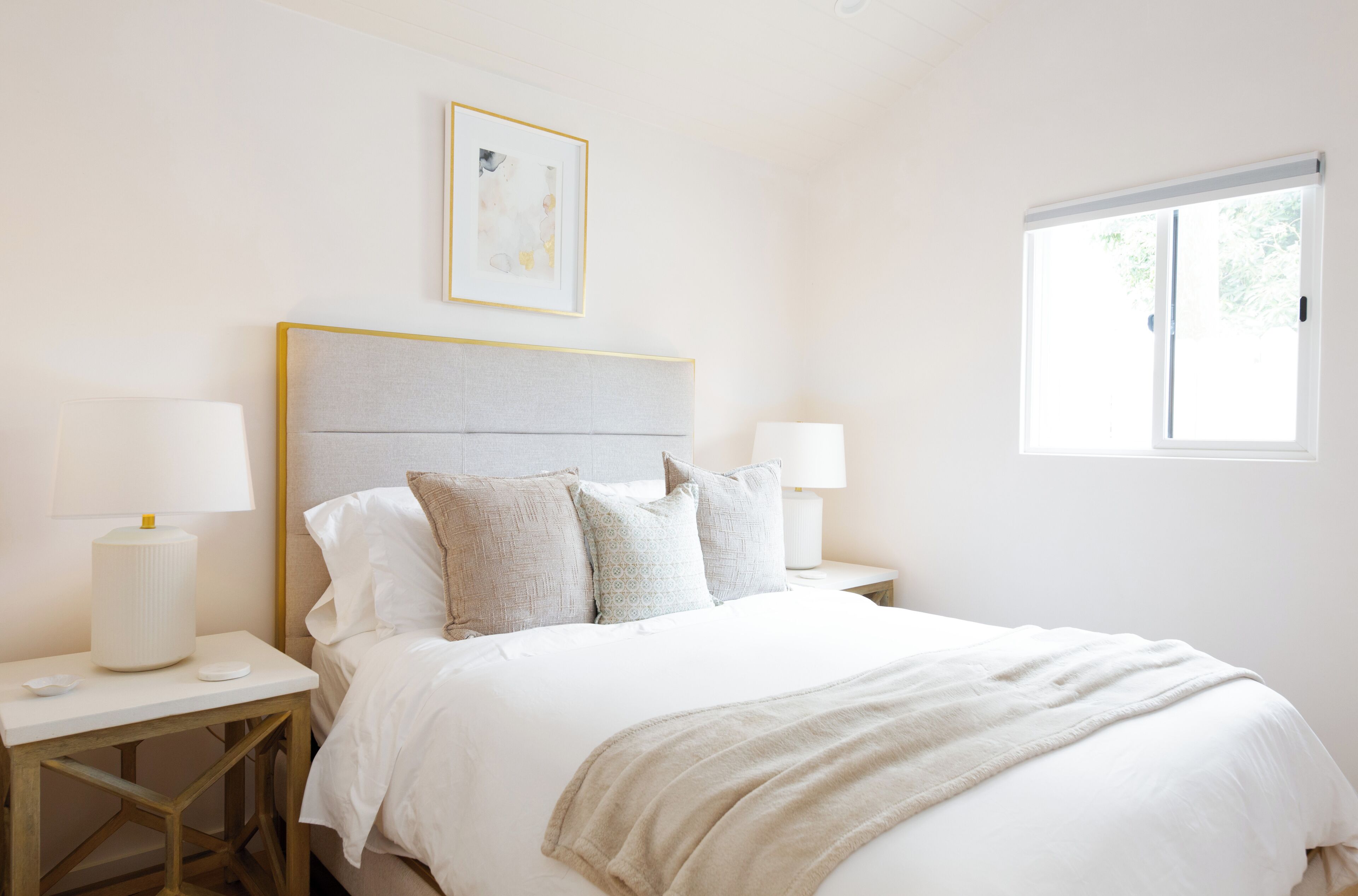 A bedroom with a bed, nightstands, lamps, a window, and a framed picture on the wall.
