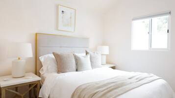 A bedroom with a bed, nightstands, lamps, a window, and a framed picture on the wall.