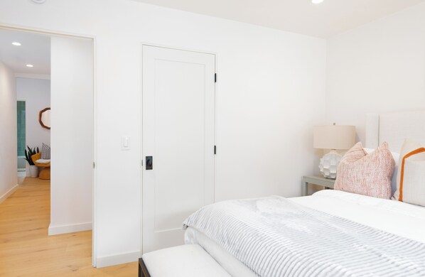 A bedroom with a bed, bedside table, lamp, and a door leading to another room.