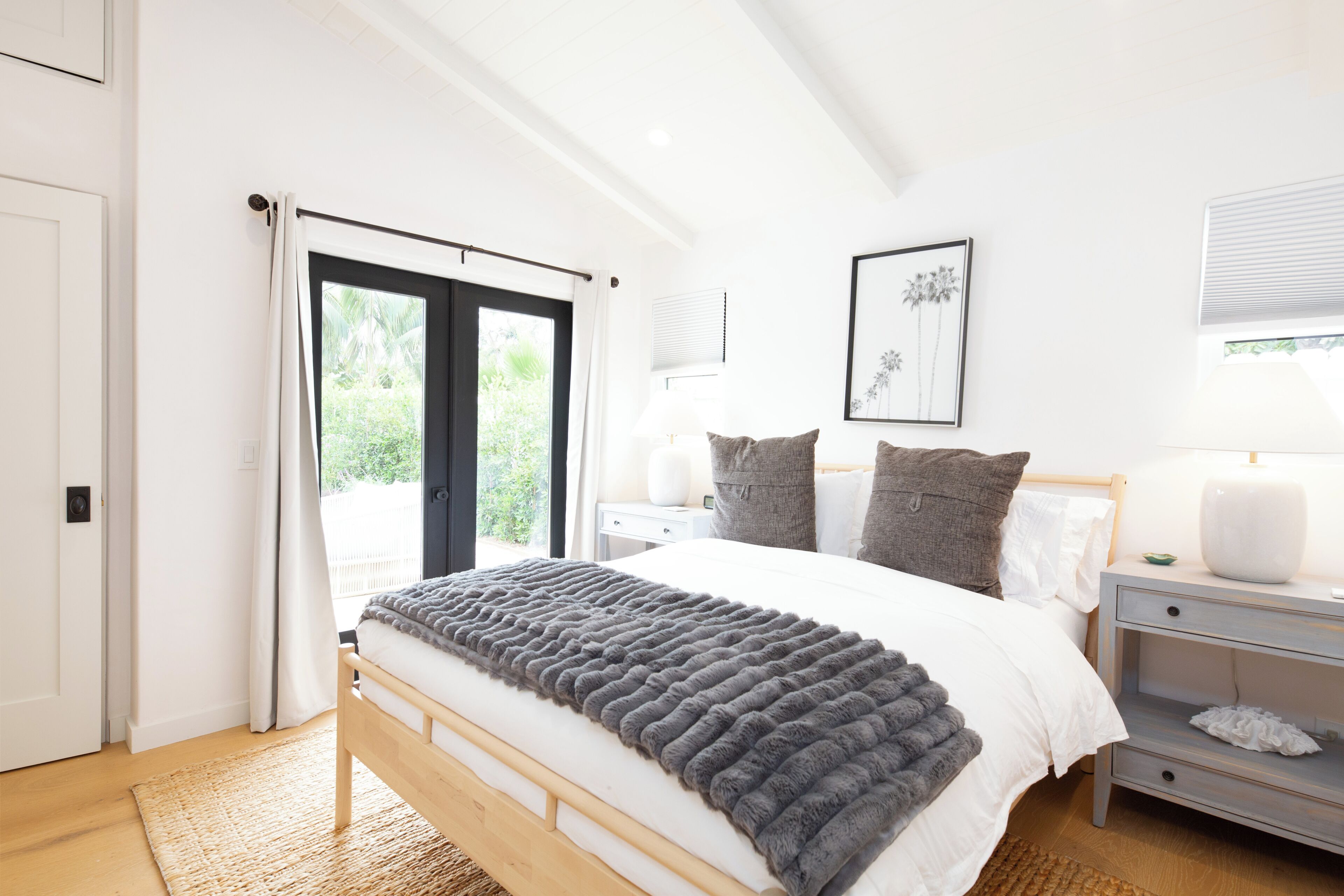 Une chambre à coucher comprenant un lit, des tables de chevet, une commode, une fenêtre avec des rideaux et un tableau encadré accroché au mur.