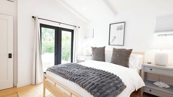 Une chambre à coucher comprenant un lit, des tables de chevet, une commode, une fenêtre avec des rideaux et un tableau encadré accroché au mur.