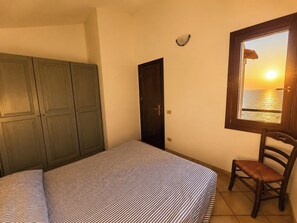 A bedroom with a bed, a chair, a wardrobe, a door, and a window with a view of the sea. - Villa with panoramic ocean views and private pools (Trinità d'Agultu e Vignola)