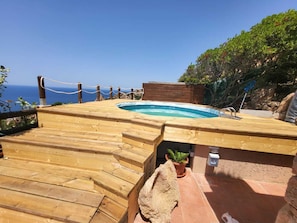 Une terrasse en bois avec un jacuzzi, une plante en pot et une vue sur l’océan.