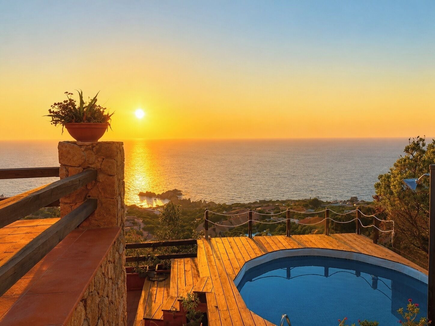 A wooden deck with a pool, overlooking a coastal view during sunset.