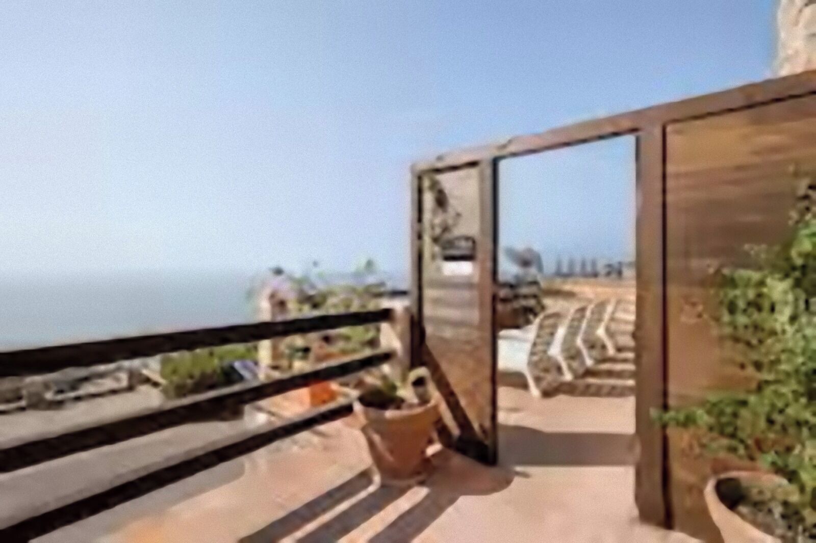 A balcony with a view of the sea, a wooden door, and potted plants.