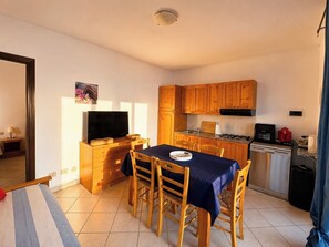 A compact kitchen with wooden cabinets, a dining table with chairs, a television, and a small refrigerator. - Villa with panoramic ocean views and private pools (Trinità d'Agultu e Vignola)