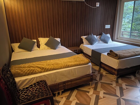 A hotel room with two beds, a wooden floor, and a window with a view of greenery.