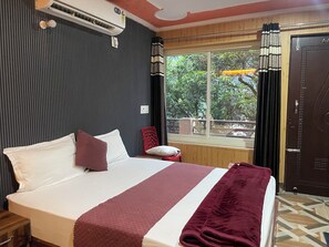 A hotel room with a bed, a window with curtains, a door, and a radiator.