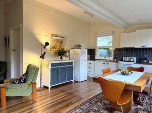 A modern kitchen with white cabinets, a dining area with a wooden table, and a patterned rug. - Apple Tree Cottage, a charming mid century hideaway close to town and bushwalks (Blackheath)