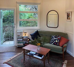 A cozy living room with a green sofa, a coffee table with a vase, and a bookshelf. - Apple Tree Cottage, a charming mid century hideaway close to town and bushwalks (Blackheath)