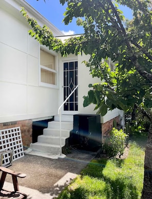 Una casa de dues plantes amb façana blanca, una porta amb un panell de vidre i una escala de formigó que condueix a una porta de color fosc.
