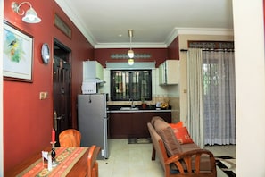 A compact living space with a kitchenette, dining area, and a sofa with cushions. - Malachite Birdsong Retreat Apt 3 (Kampala)