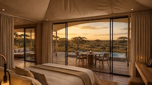 Un dormitorio con una cama grande, un escritorio y vistas a una terraza exterior con piscina y paisaje natural.