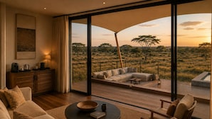 Una sala de estar moderna con un gran ventanal corredero que da a una terraza exterior con vistas a un paisaje de sabana.