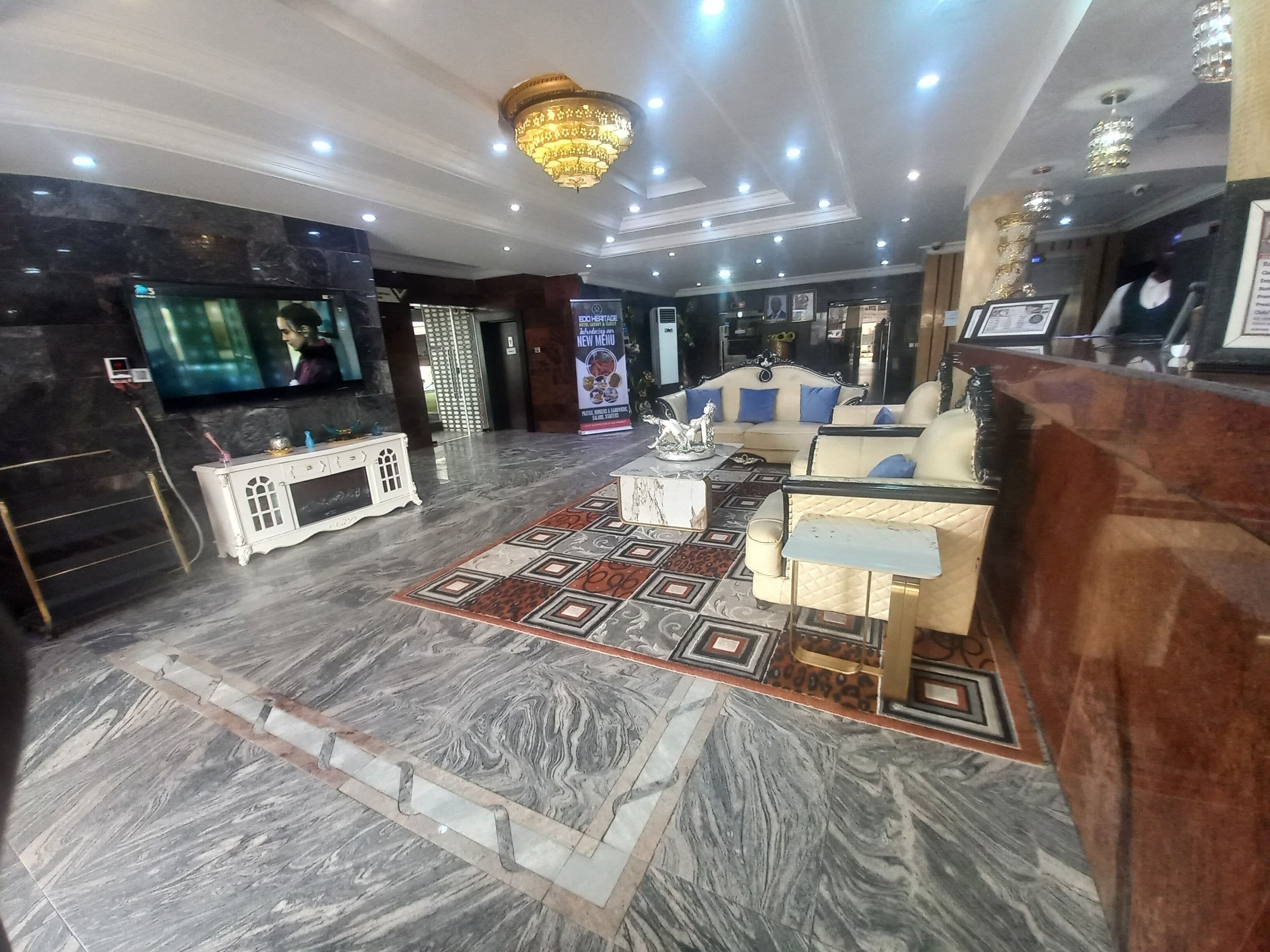 A hotel lobby with a marble floor, a reception desk, a sofa, and a chandelier.