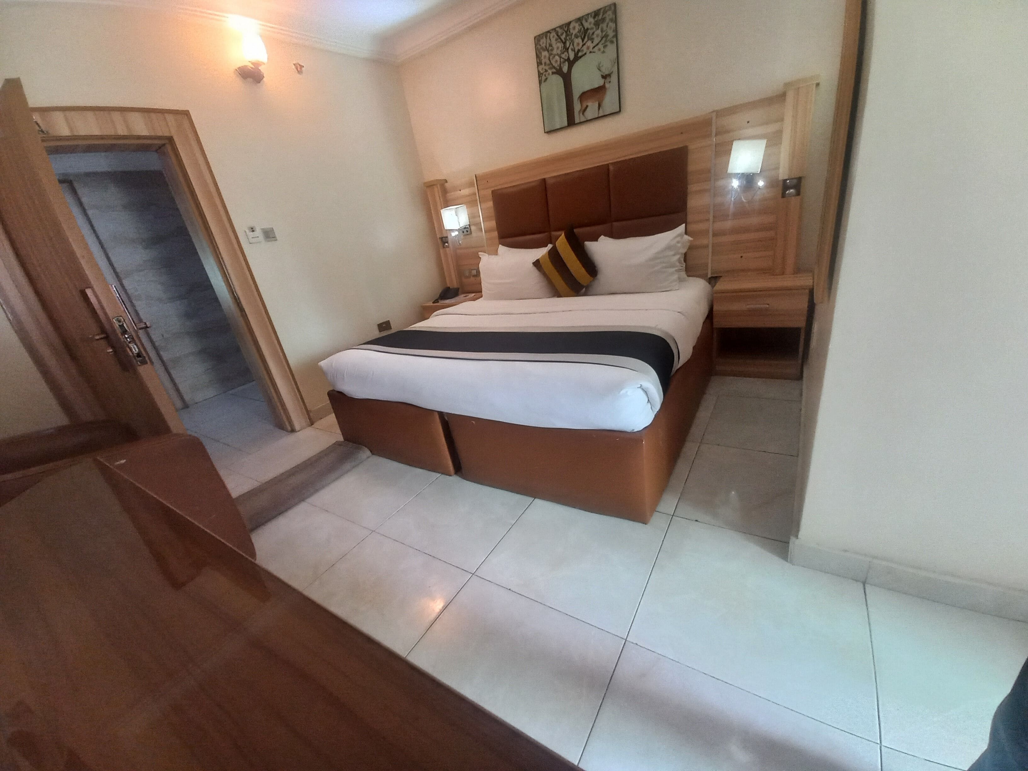 A hotel room with a bed, bedside table, and a door leading to a hallway.
