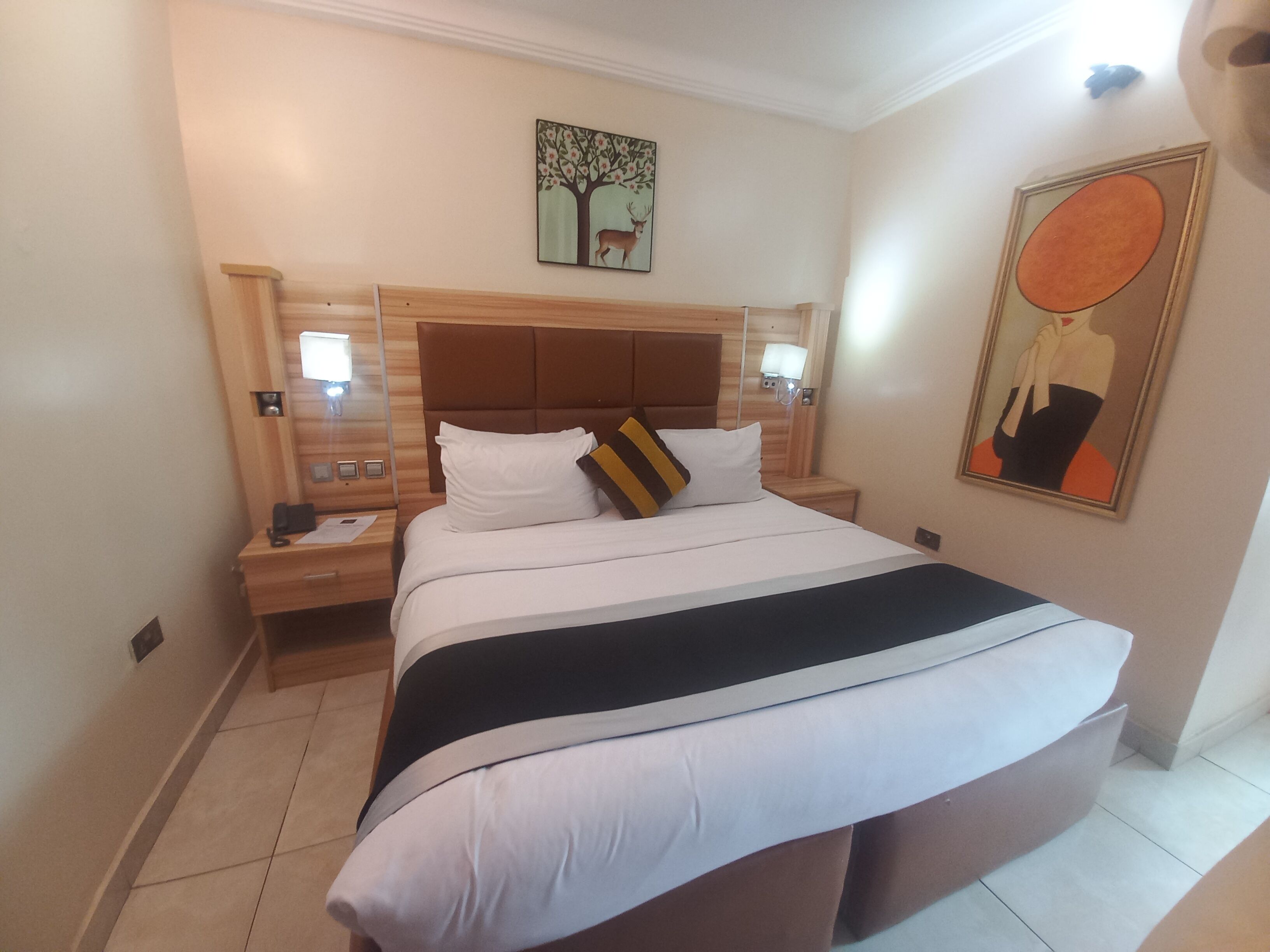 Una camera d'albergo con un letto grande, una testiera in legno, lampade ai comodini e opere d'arte alle pareti.