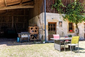 A rustic outdoor area with a wooden table and chairs, a barbecue grill, and a covered storage space.
