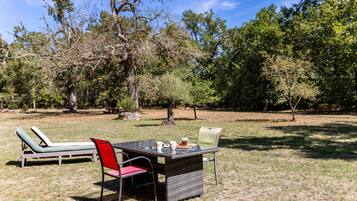 An outdoor seating area with a table and chairs, surrounded by trees.