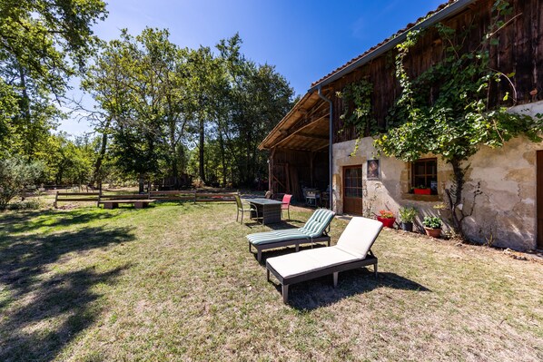 A rustic outdoor seating area with two lounge chairs and a table, surrounded by a wooden fence and trees.