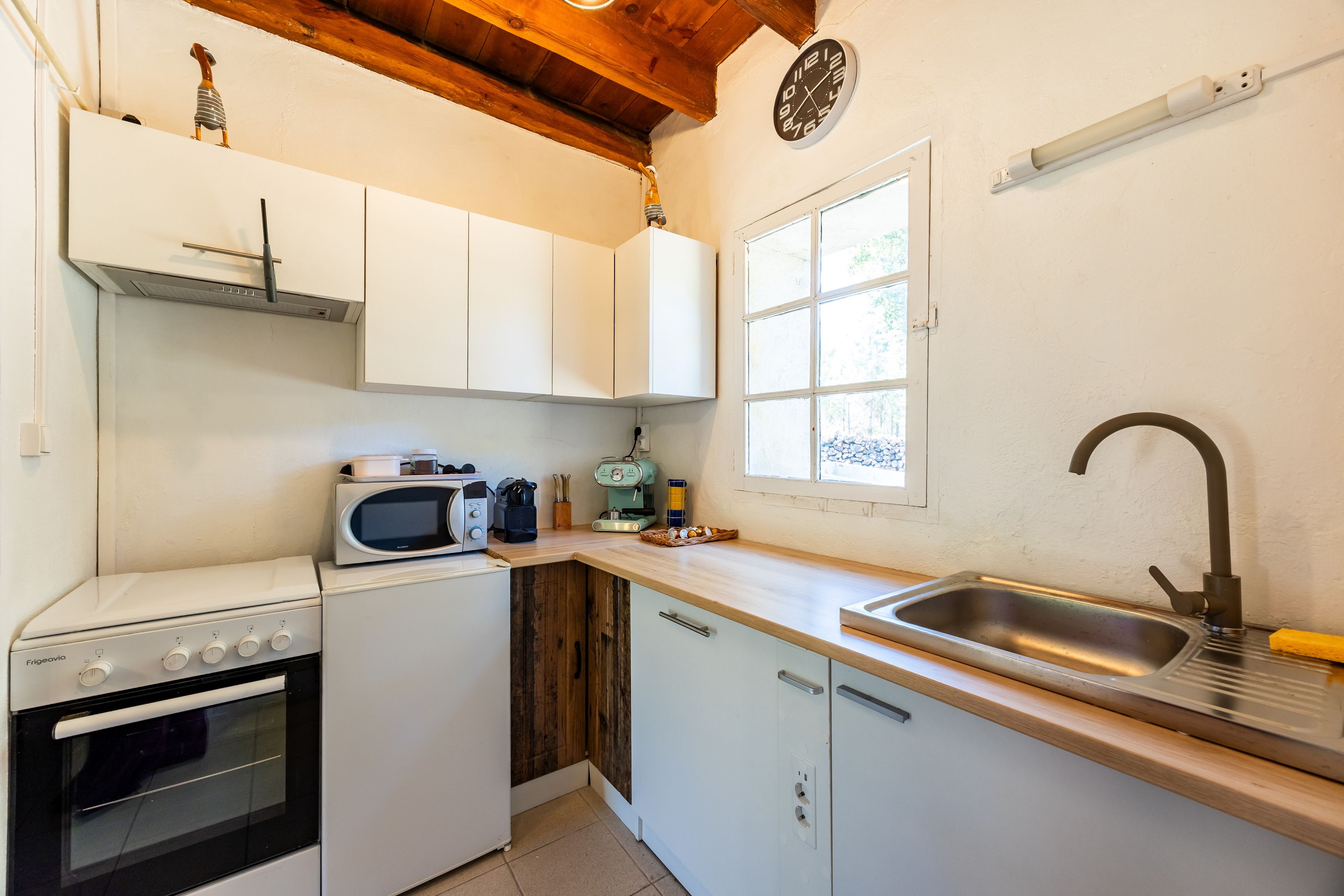 A compact kitchen with white cabinets, a microwave, a stove, a sink, and a window.
