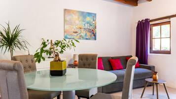 Una sala de estar con una mesa de vidrio, sillas, sofá, un cuadro y una ventana con cortinas.