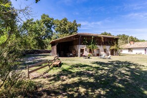 A rustic barn with a covered porch, a wooden bench, and a table with chairs.