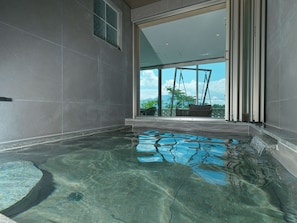 Piscina interna com água cristalina, vista para o exterior através de uma grande janela e área de estar com vista.