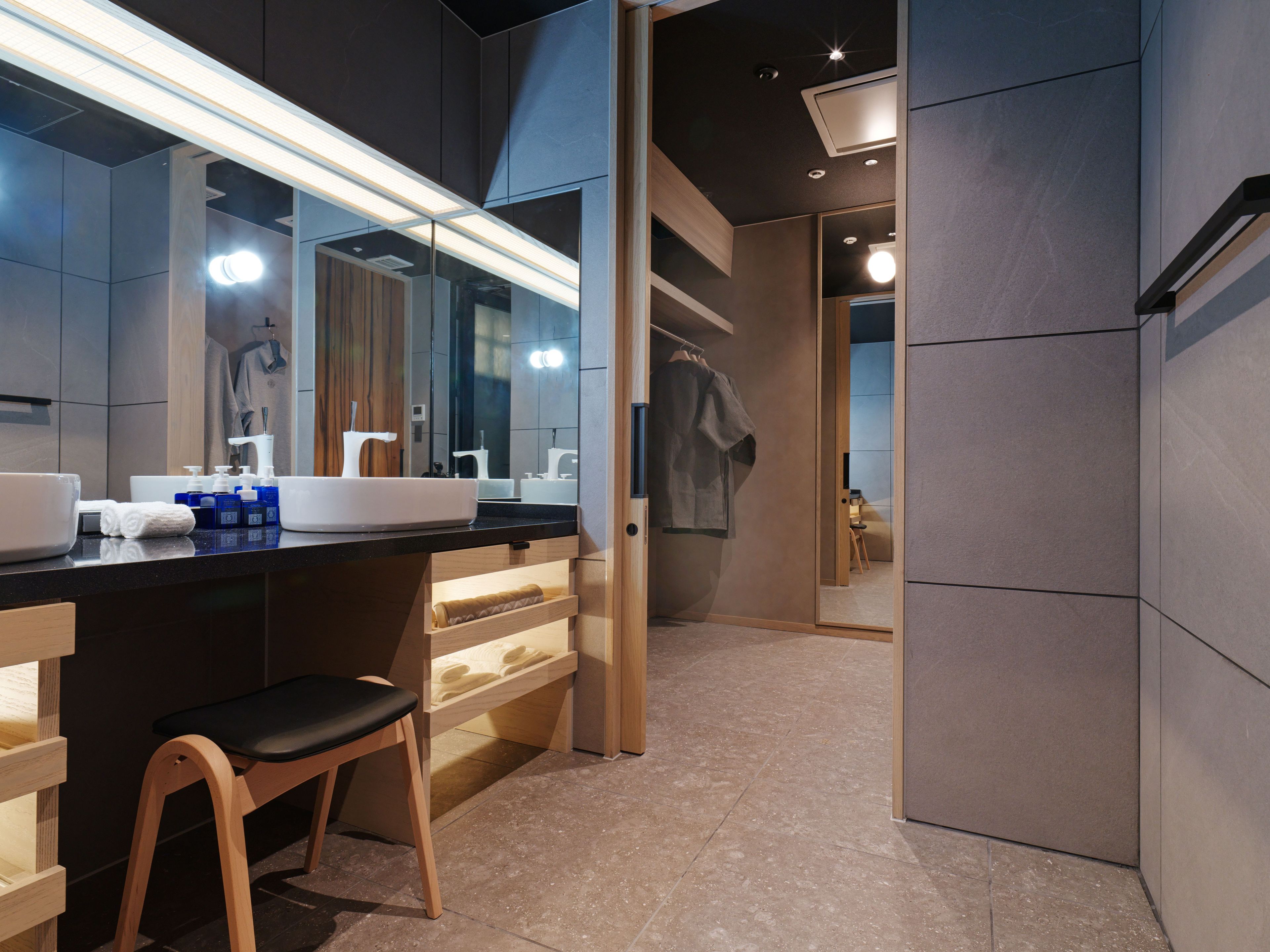 A modern bathroom with a large mirror, dual sinks, and a wooden chair.