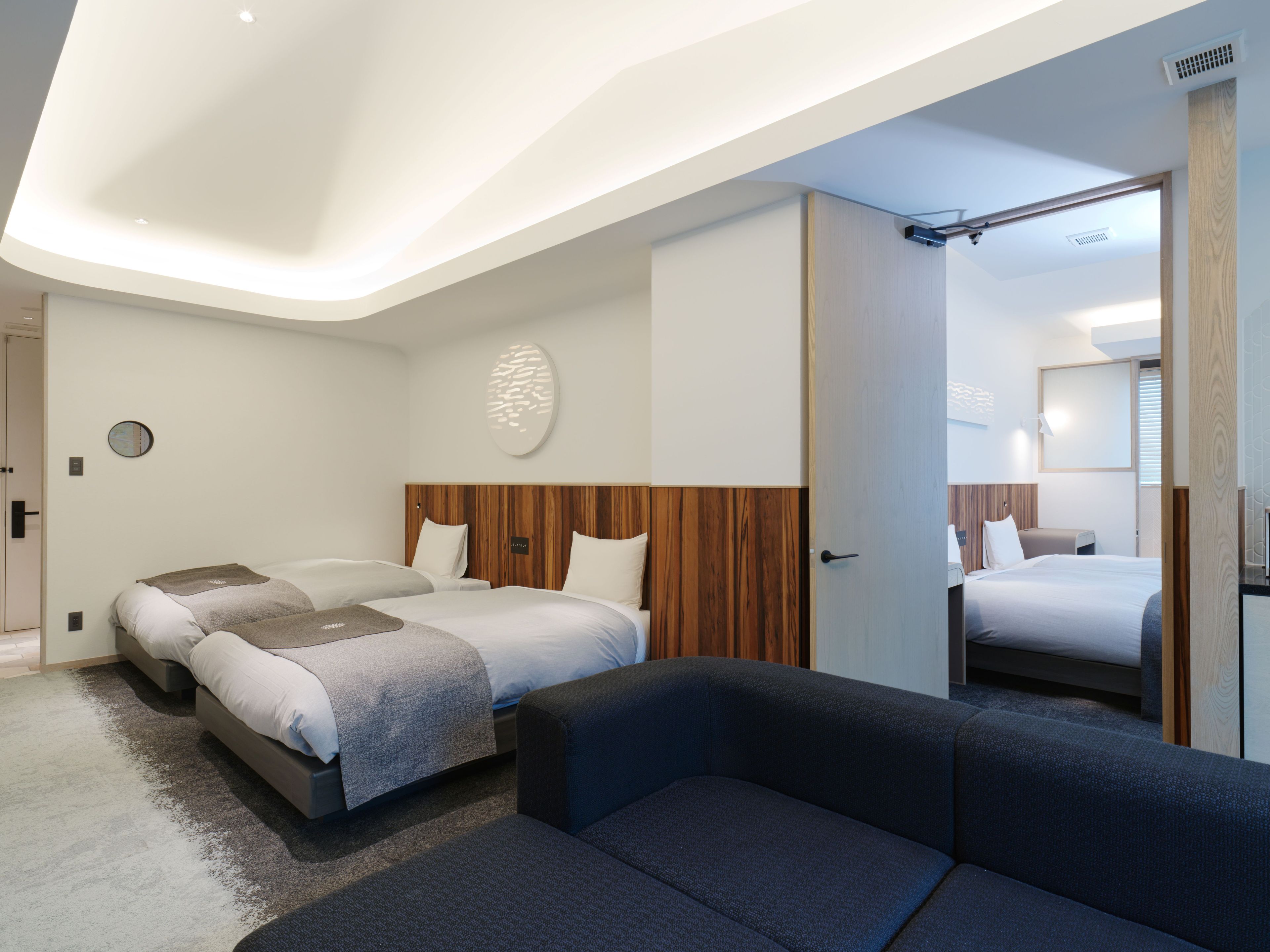 Une chambre d’hôtel moderne avec un grand lit, deux petits lits, un canapé et un miroir.