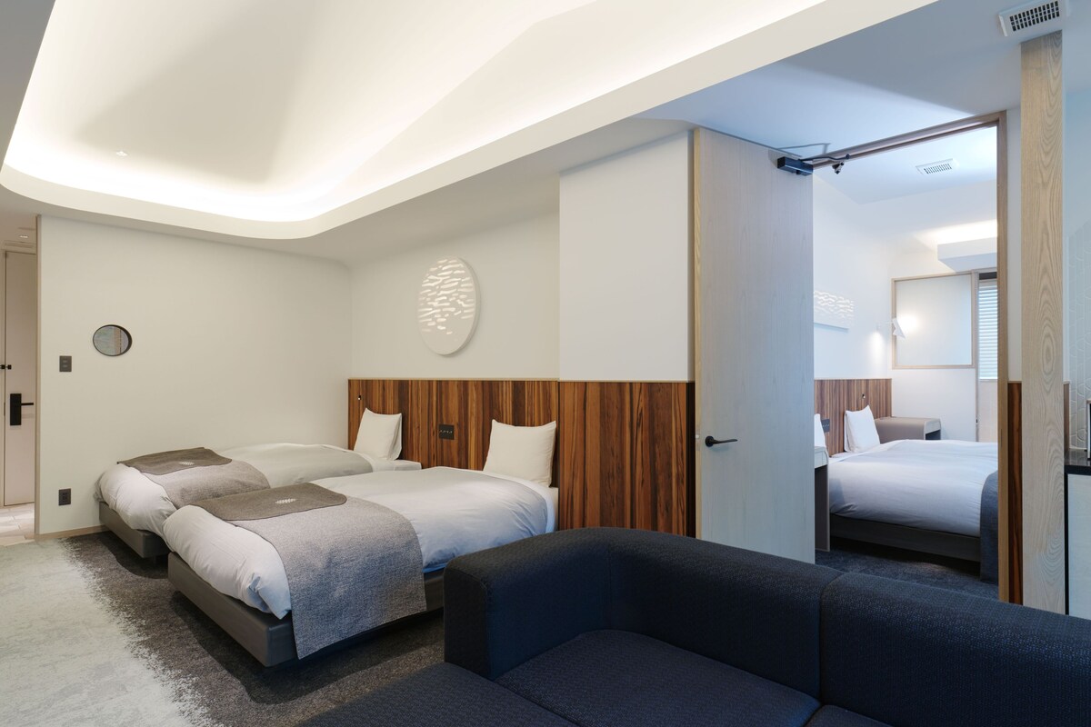 Quarto de hotel moderno com uma cama grande, duas camas menores, um sofá e um espelho.