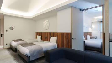 Une chambre d’hôtel moderne avec un grand lit, deux petits lits, un canapé et un miroir.