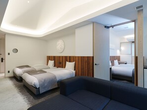 A modern hotel room with a large bed, two smaller beds, a sofa, and a mirror.