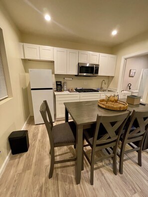 A compact kitchen with white cabinets, a microwave, a refrigerator, and a dining table with chairs. - Brand New Private ADU (Los Angeles)