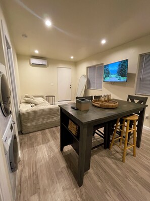 Un espacio habitable compacto con kitchenette, comedor con mesa y sillas, cama y televisor montado.