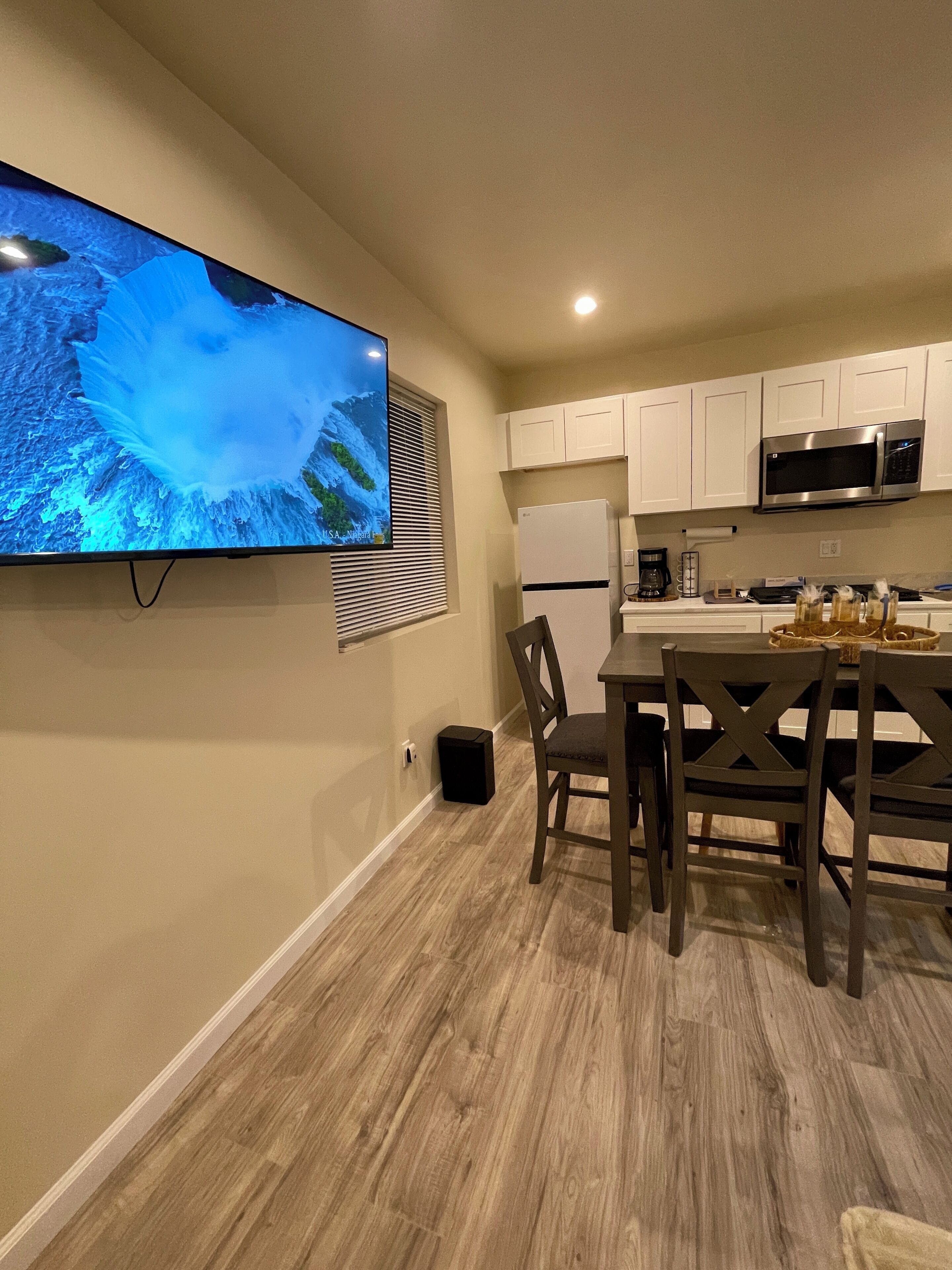 Una cocina moderna con armarios blancos, un microondas de acero inoxidable y un televisor de pantalla plana montado en la pared.