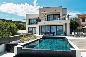 Ein modernes, zweistöckiges Haus mit Swimmingpool, Gartenmöbeln und Blick auf die umliegende Landschaft.