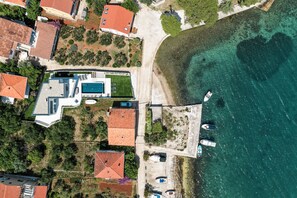 Luftaufnahme eines Küsteneigentums mit Schwimmbad, mehreren Booten und Strand.