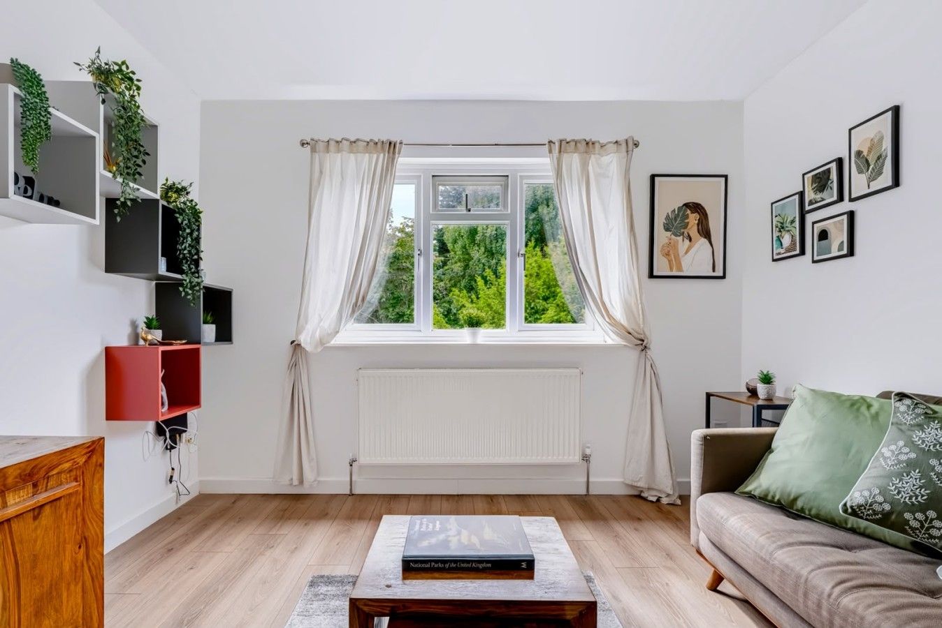Una sala de estar con ventana, radiador, sofá, mesa de centro y estanterías con plantas.